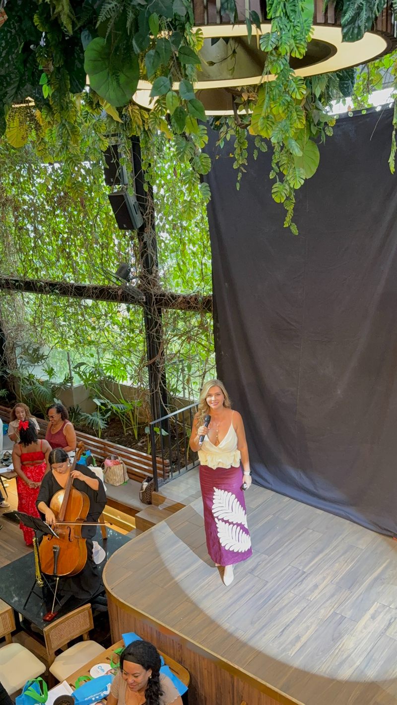 Lina Hernández con micrófono en el escenario de un encuentro de Mujeres Invencibles, acompañada por una violonchelista en vivo